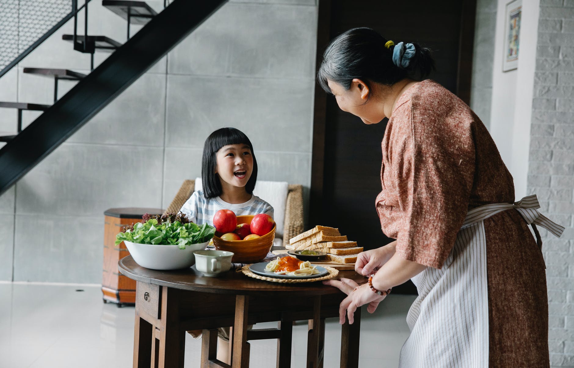 happy ethnic elderly woman serving healthy lunch for cute granddaughter
